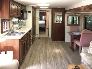 A compact RV interior with a kitchenette, a dining area, and a small seating space.