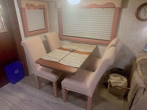 Un pequeño comedor con una mesa y cuatro sillas, un cubo de basura azul y un reloj en la pared.
