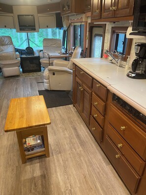 Interior compacto de una caravana con kitchenette, zona de estar y una pequeña mesa con libros.