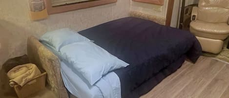 A bedroom with a bed, a chair, a bedside table, and a wall-mounted light fixture.