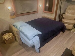 A bedroom with a bed, a chair, a bedside table, and a wall-mounted light fixture.