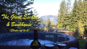 A hot tub with a bottle of wine and glasses, surrounded by trees and a mountain view. - The Great Escape - Port Renfrew & Bunkhouse (Port Renfrew)
