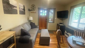 A living room with a sofa, ottoman, wooden coffee table, and a television.