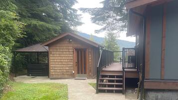 A wooden cabin with a porch and a deck, surrounded by trees and a mountain backdrop.