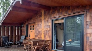 A wooden deck with a table and chairs, a sliding glass door leading to a fire pit area. - The Great Escape - Port Renfrew (Port Renfrew)