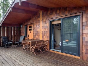 A wooden deck with a table and chairs, a sliding glass door leading to a fire pit area.