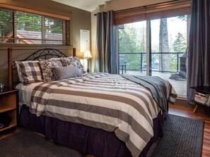 A bedroom with a large bed, a nightstand, a lamp, and a view of the outdoors through a window.