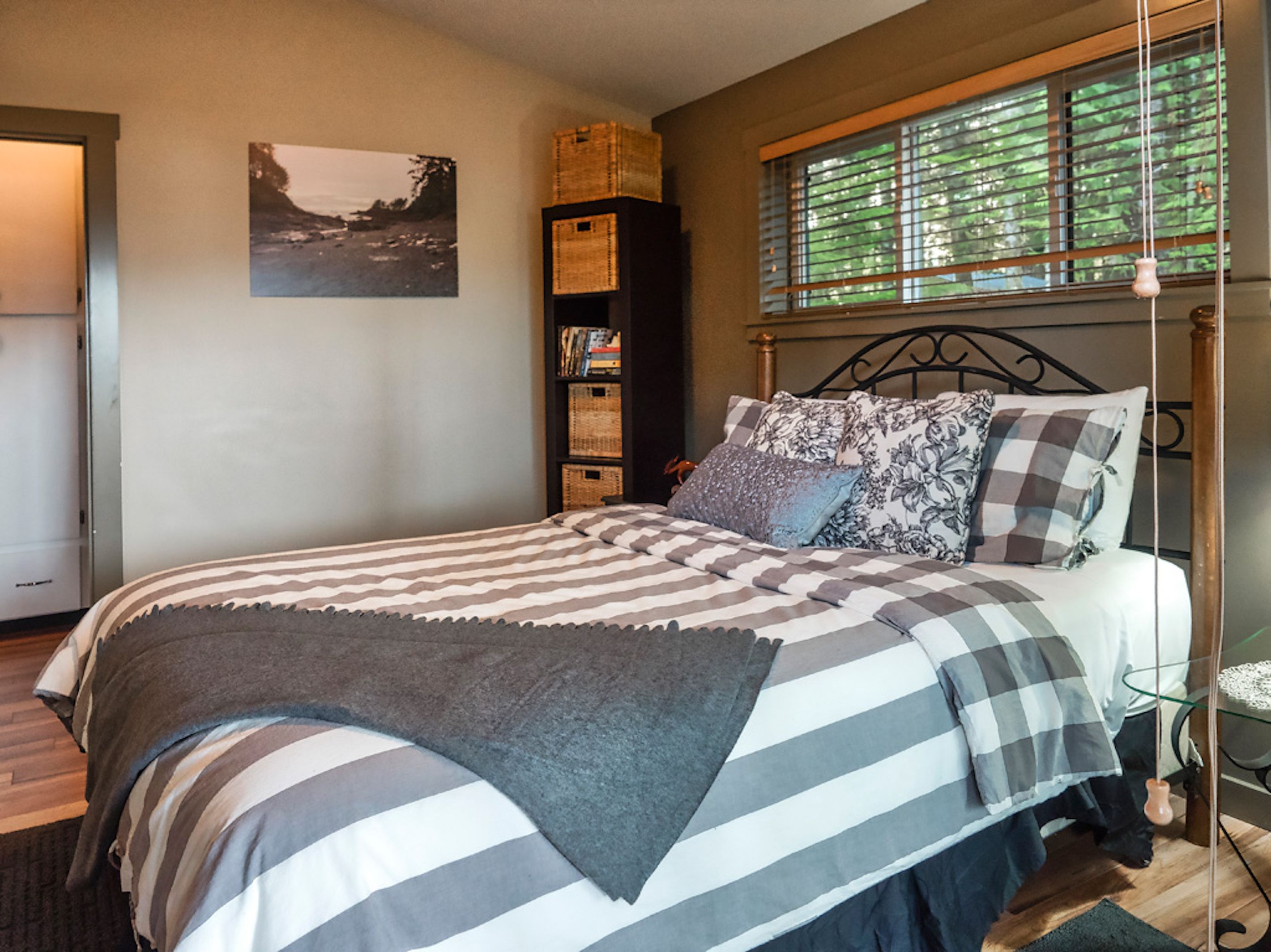 A bedroom with a bed, a window with blinds, a bookshelf, and a wall-mounted picture.