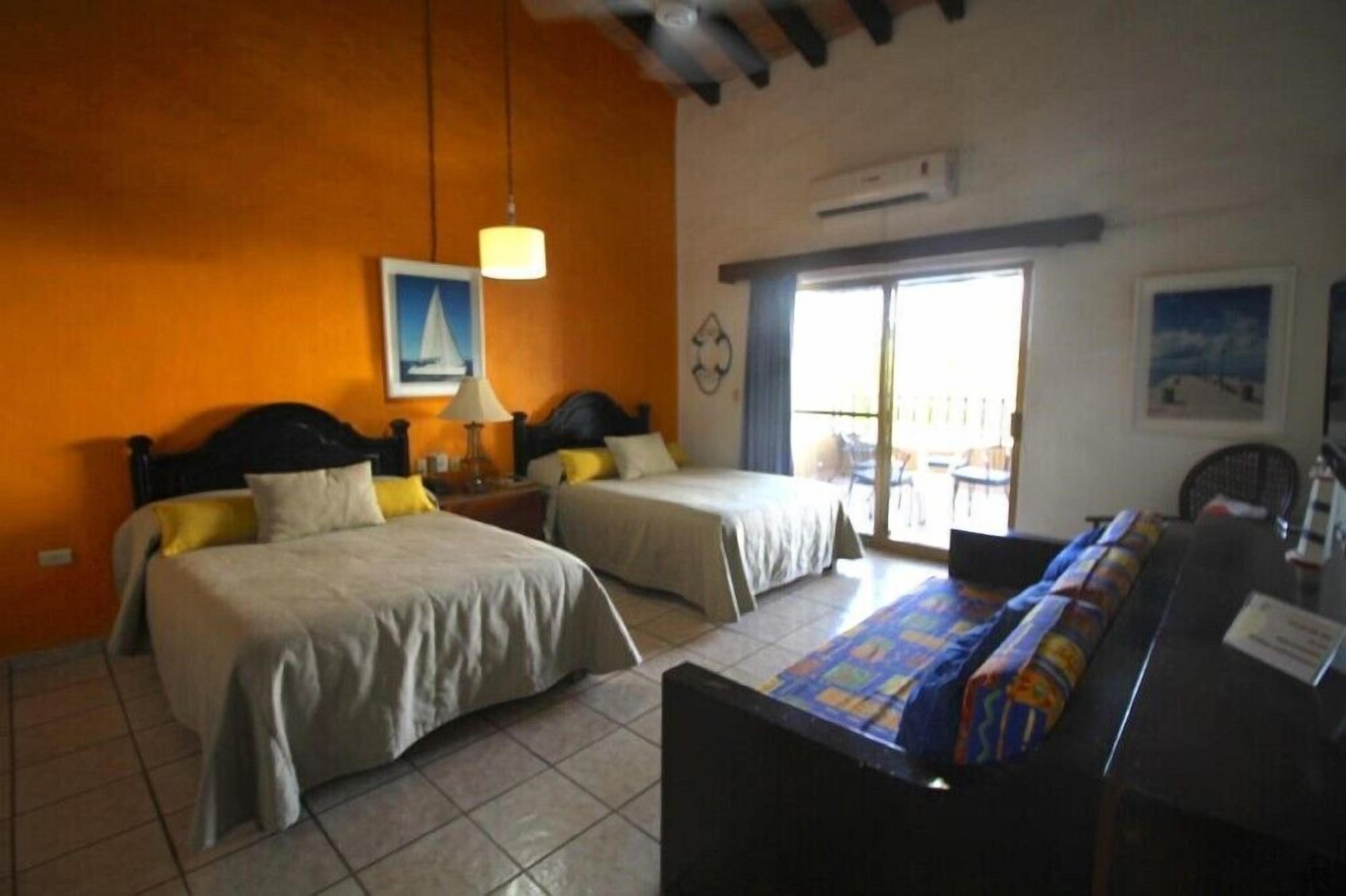 A hotel room with two beds, a desk, and a view of the outside.