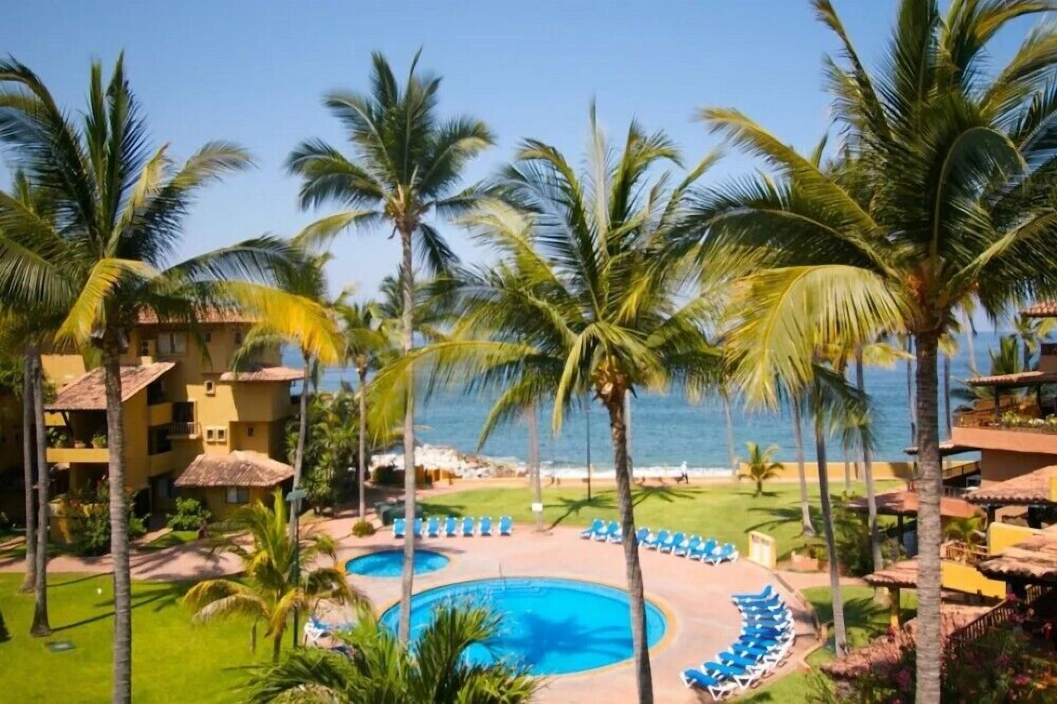 Un resort con piscina, palmeras y vista al océano.