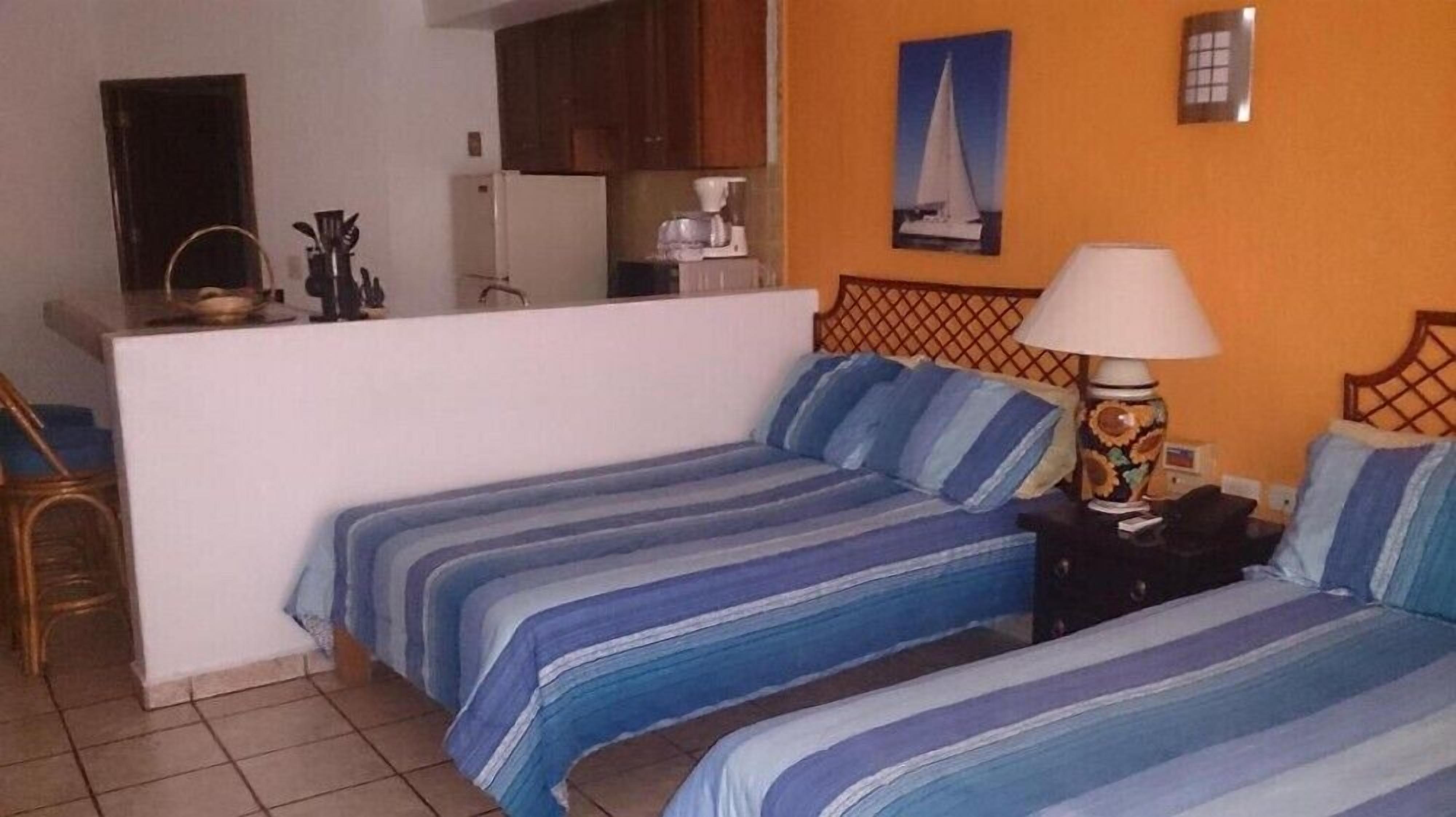 Une chambre avec deux lits, une petite kitchenette, une machine à café et un tableau représentant un voilier accroché au mur.