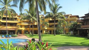 Un hotel con varios balcones, piscina y abundante vegetación.