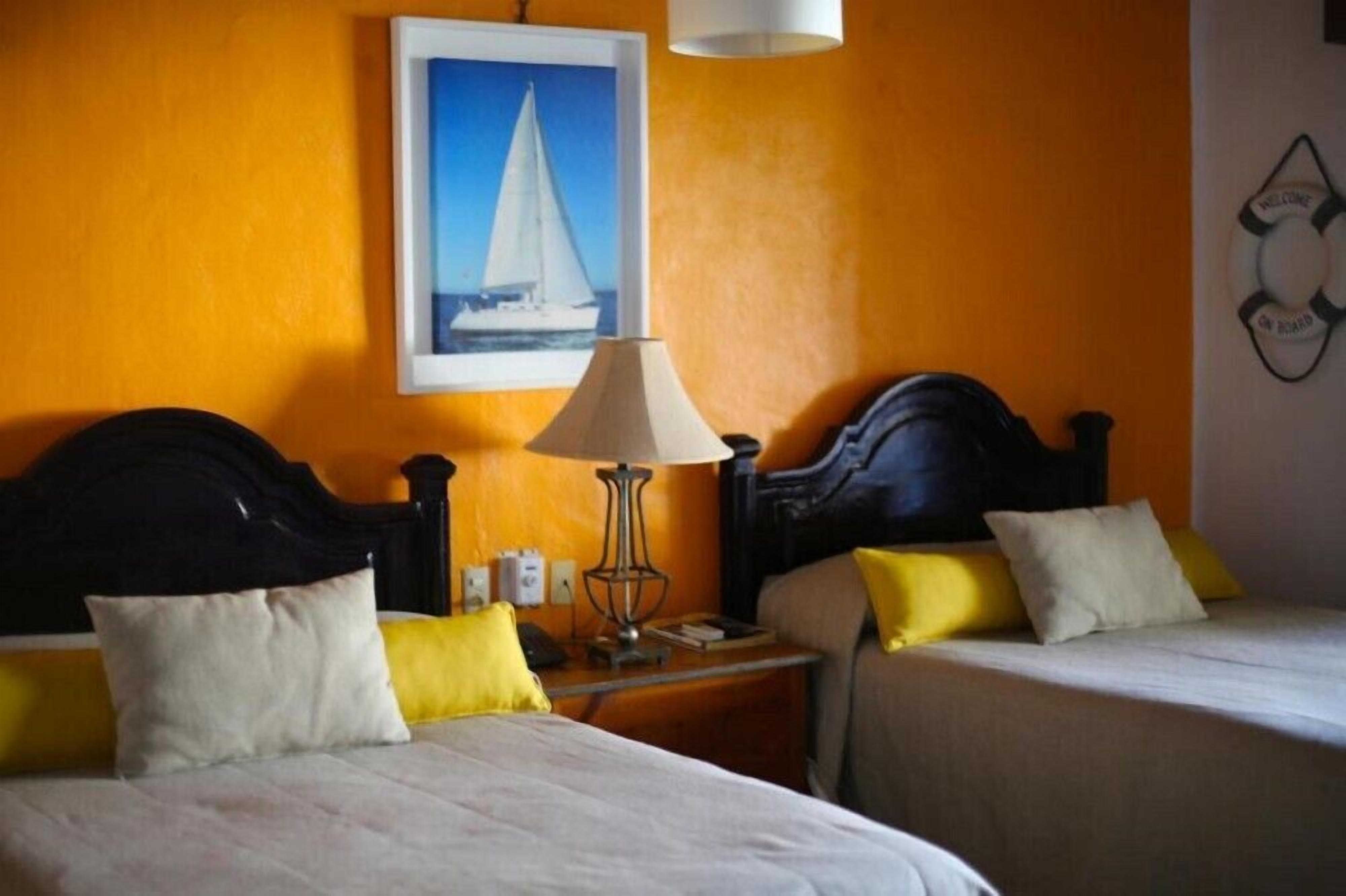 Une chambre d’hôtel avec deux lits, une table de chevet avec une lampe et un tableau représentant un voilier accroché au mur.