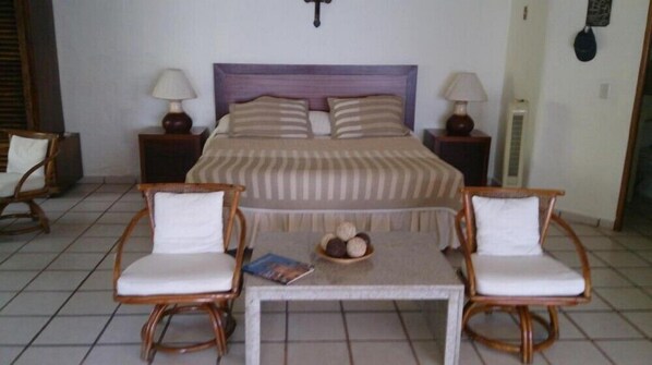 A bedroom with a bed, two nightstands, two bedside lamps, a wooden table with chairs, and a small decorative item on the table.