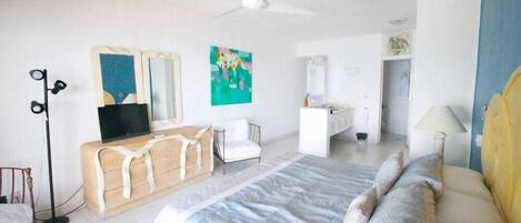 A bedroom with a bed, bedside table, a mirror, a ceiling fan, and a TV.