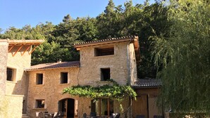 Un edificio de piedra con un patio, mobiliario exterior y una pérgola cubierta de enredaderas.