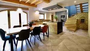 Una cocina moderna con vigas de madera, un comedor con mesa y sillas, y una escalera que conduce a una chimenea de piedra.