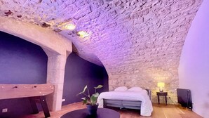 Una habitación acogedora con techo de piedra, una cama, una mesita y un banco.