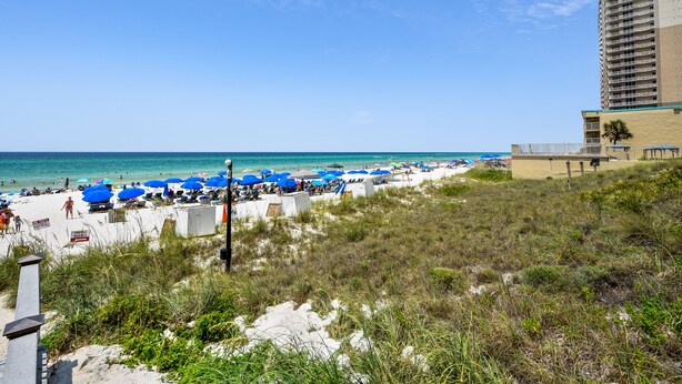 A beach with blue umbrellas, a sandy shore, and a tall building in the background.