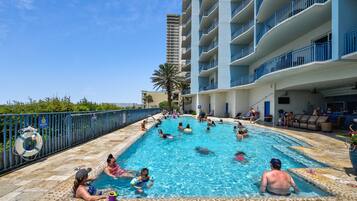 A swimming pool area with multiple levels of balconies, a lifeguard stand, and a clear sky.