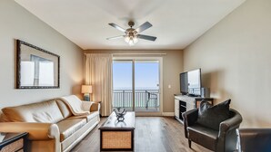 A living room with a sofa, armchair, coffee table, TV, and a balcony with a view. - Beautiful 17th Floor Views! Free Activities + Summer Deals!! (Panama City Beach)