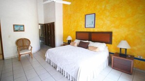 Un dormitorio con una cama, dos mesitas de noche, una silla, un ventilador de techo y un cuadro en la pared.