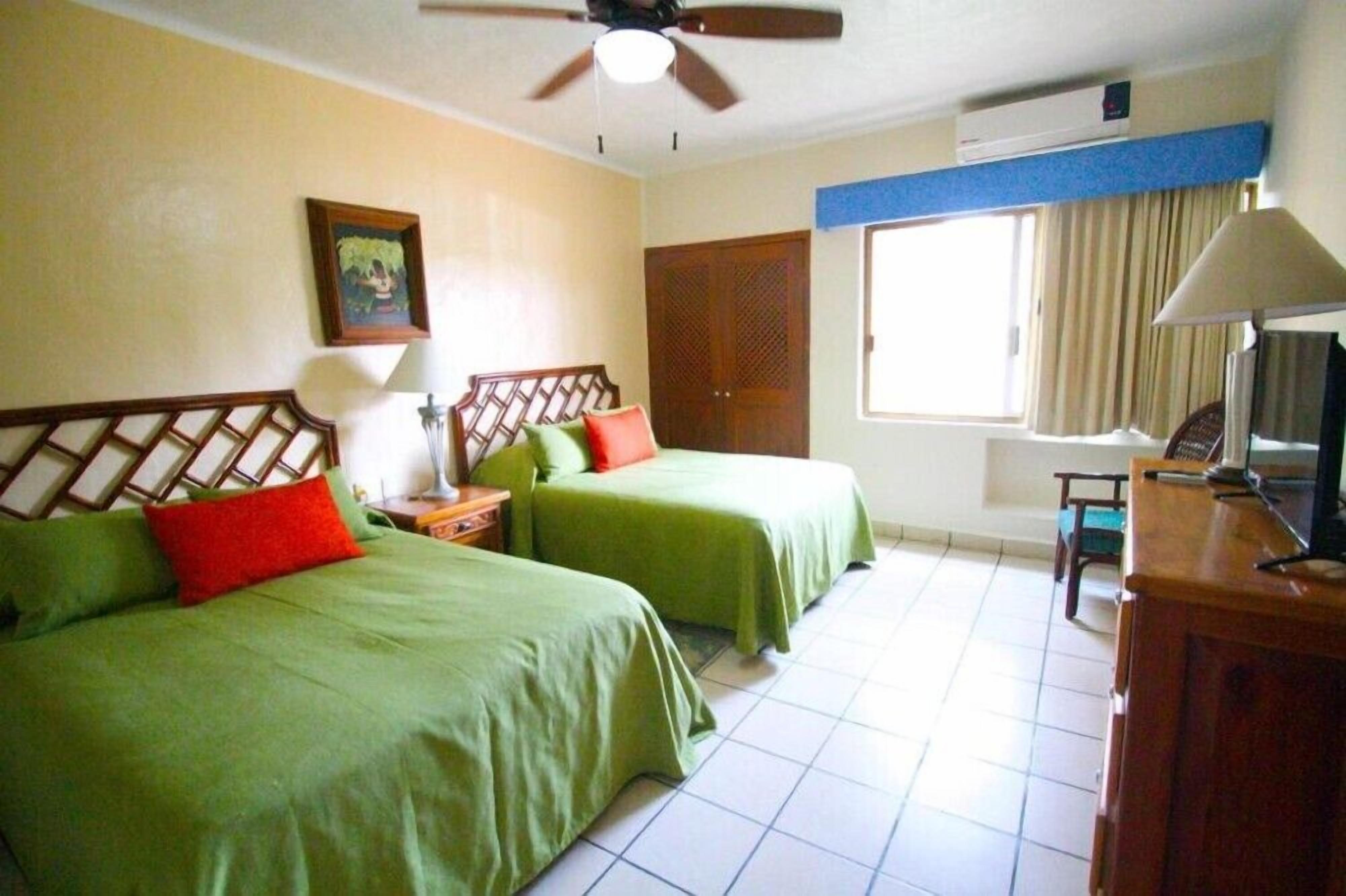 A hotel room with two beds, a ceiling fan, a TV, and a window with curtains.