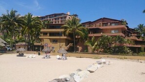 Un hôtel situé en bord de mer, avec plusieurs étages, des palmiers et des parasols de plage.