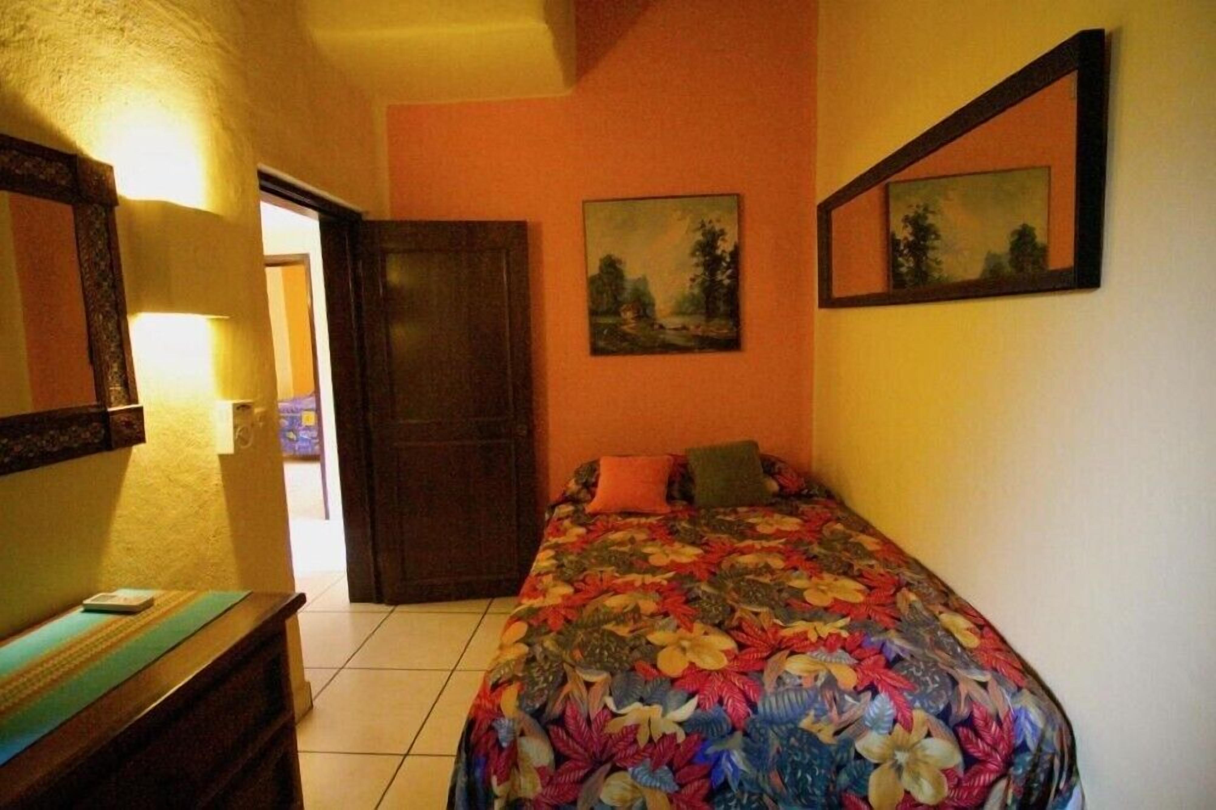 Una camera da letto con una coperta dal disegno floreale, una porta in legno e due quadri appesi al muro.