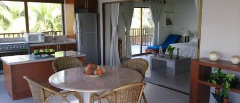A kitchen with a dining area, a refrigerator, and a view of a balcony with a chair and a table.
