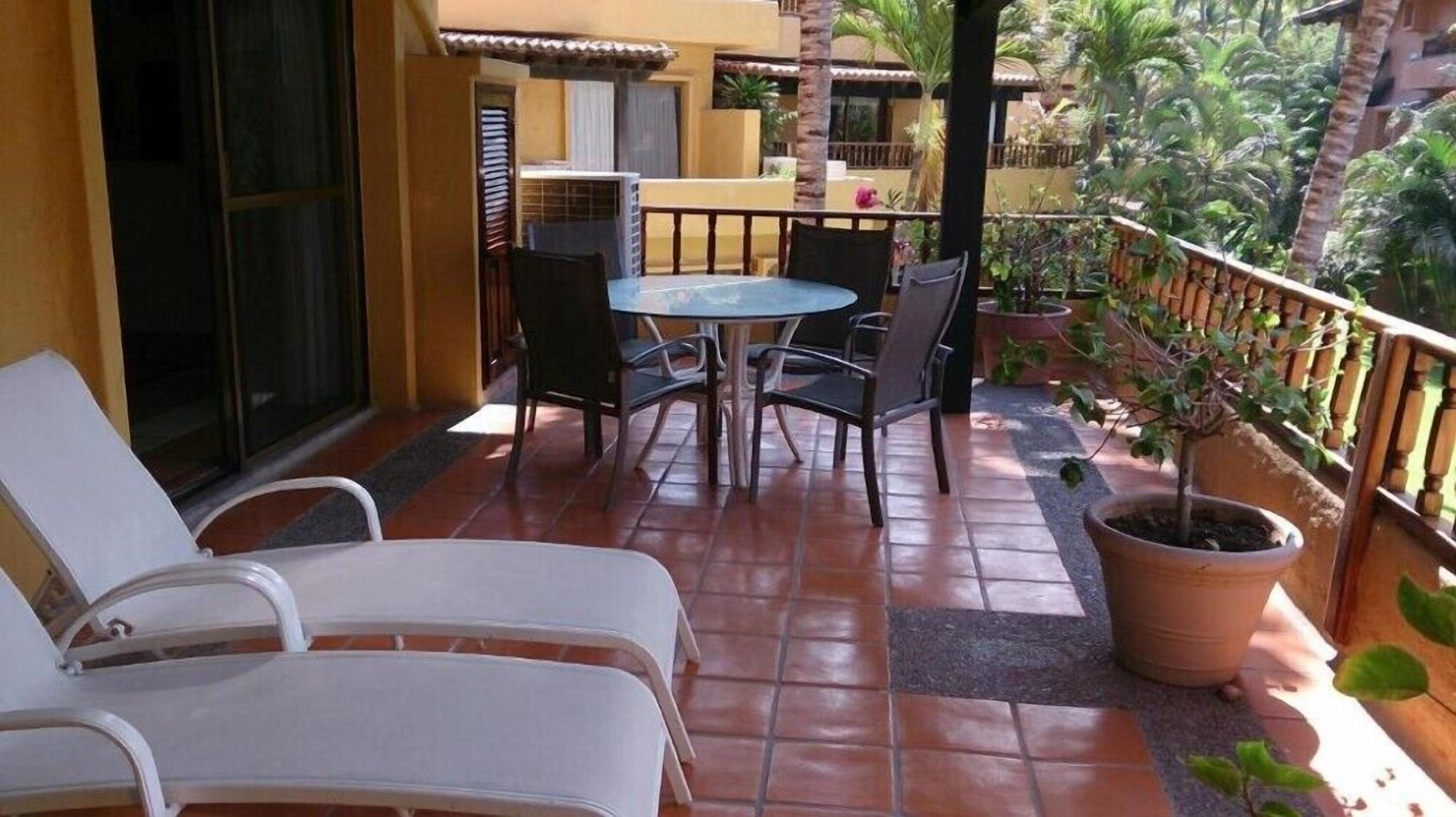 A balcony with a table and chairs, a potted plant, and a view of the surrounding area.