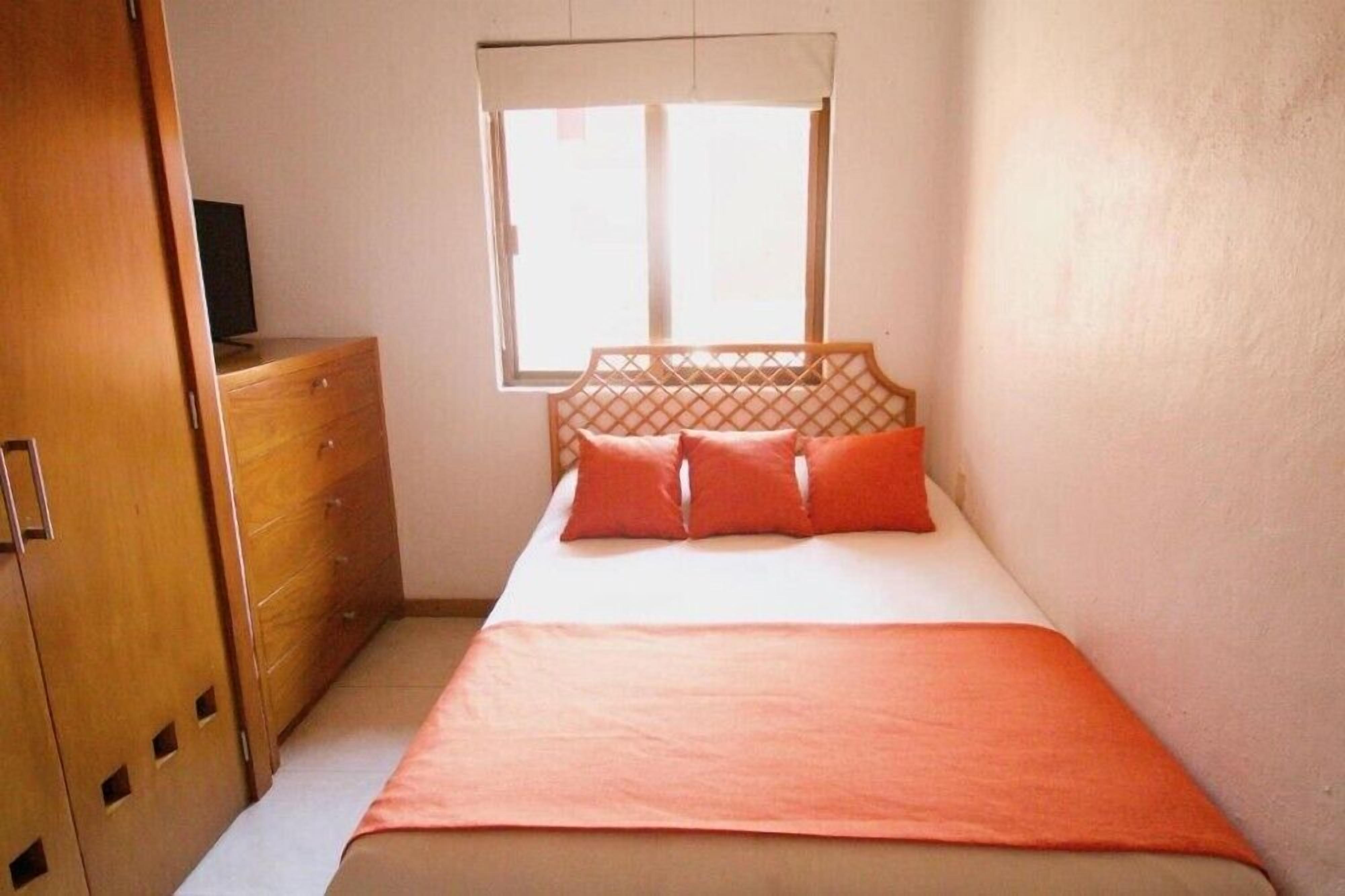 Een slaapkamer met een bed, een houten dressoir en een raam.