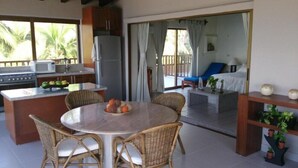 A kitchen with a dining area, a refrigerator, and a view of a balcony with a chair and a table.