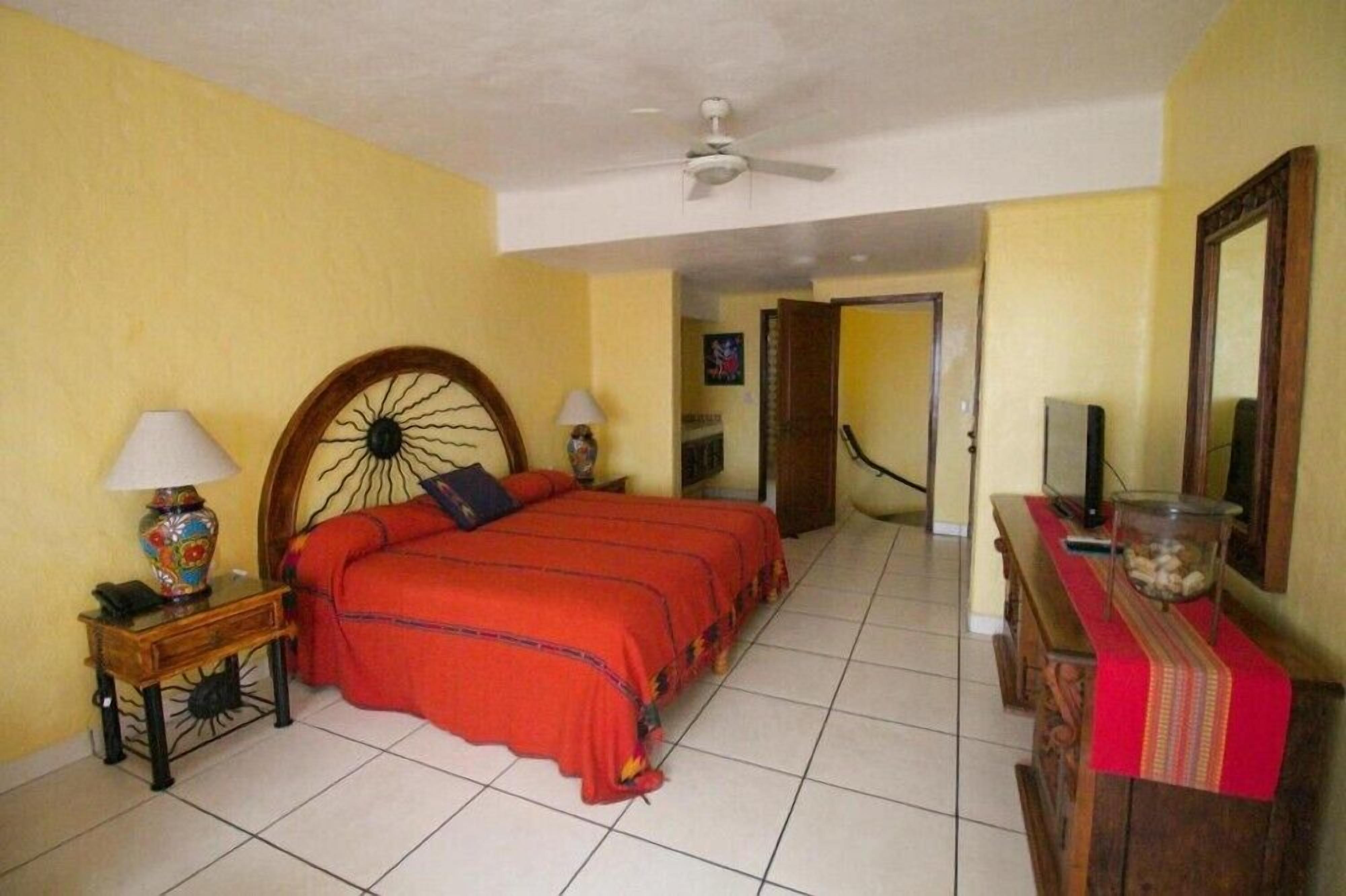 A hotel room with a large bed, two bedside tables with lamps, a television on a wooden cabinet, and a ceiling fan.