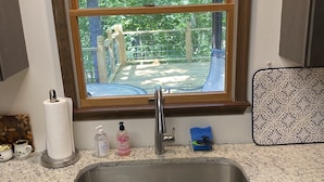Cozinha com bancada de granito, pia de aço inoxidável e janela com vista para um deck com guarda-corpo de madeira.