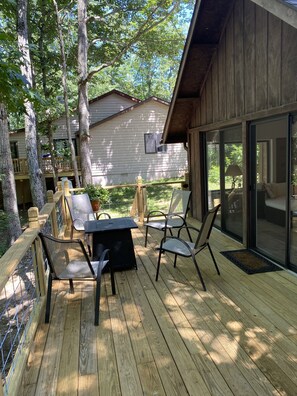 En träveranda med ett bord och stolar, med utsikt över ett hus och träd.