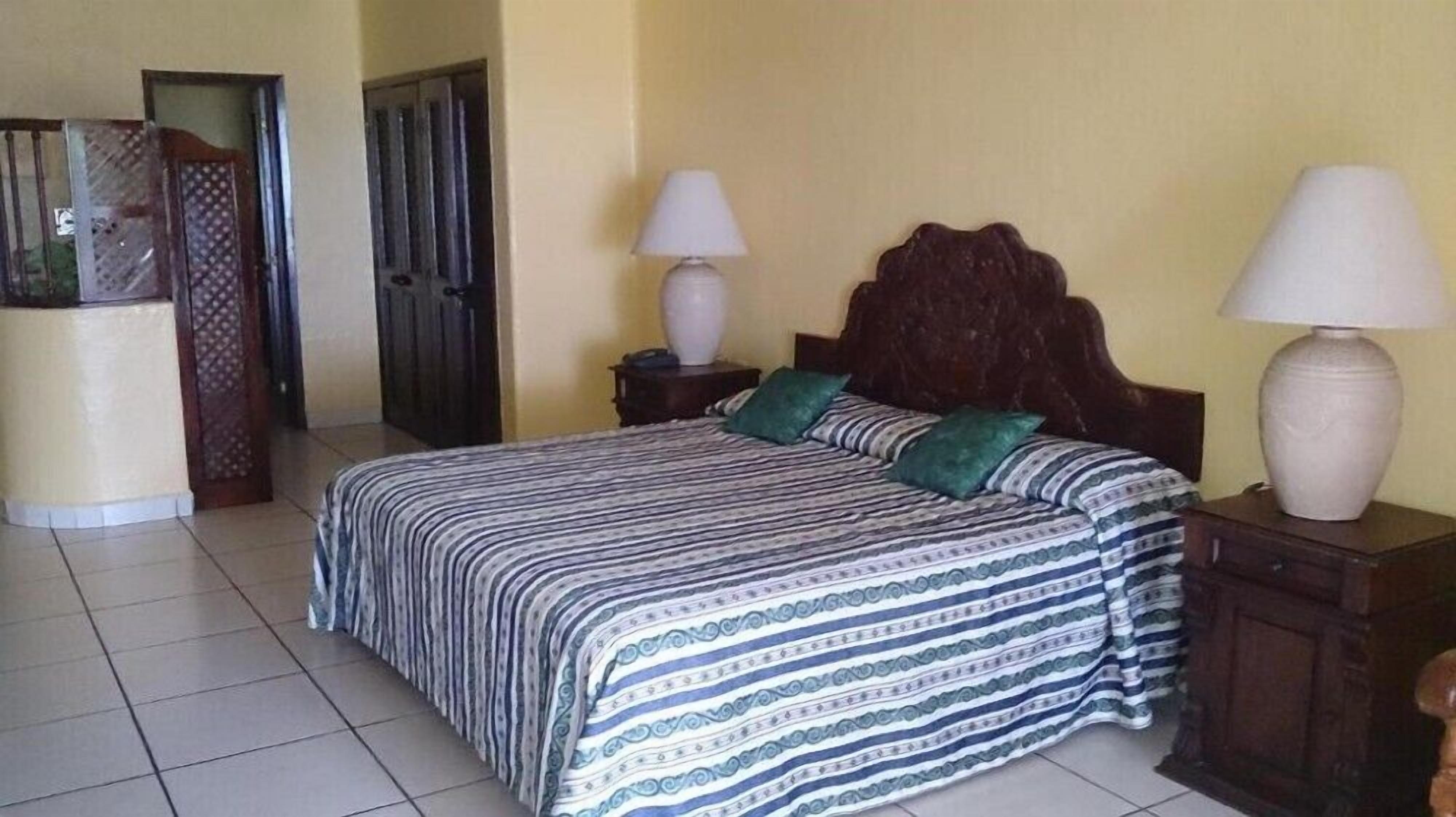 Une chambre d’hôtel comprenant un lit, deux tables de chevet, une commode, une lampe, une armoire et une porte.