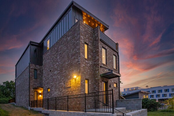 A modern multi-story building with exposed brickwork, large windows, and a black metal railing.