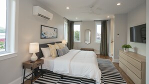 Een moderne slaapkamer met een groot bed, nachtkastjes, een flatscreen-tv en een plafondventilator.