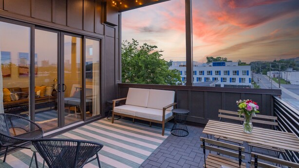 Een balkon met een bank, stoelen en een tafel, met uitzicht op een stadslandschap tijdens de zonsondergang.