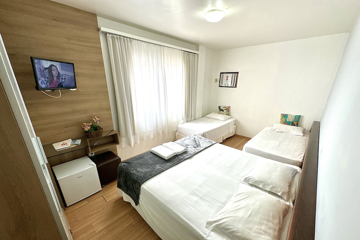 A hotel room with a large bed, a smaller bed, a desk, a chair, a television, and a window with curtains.