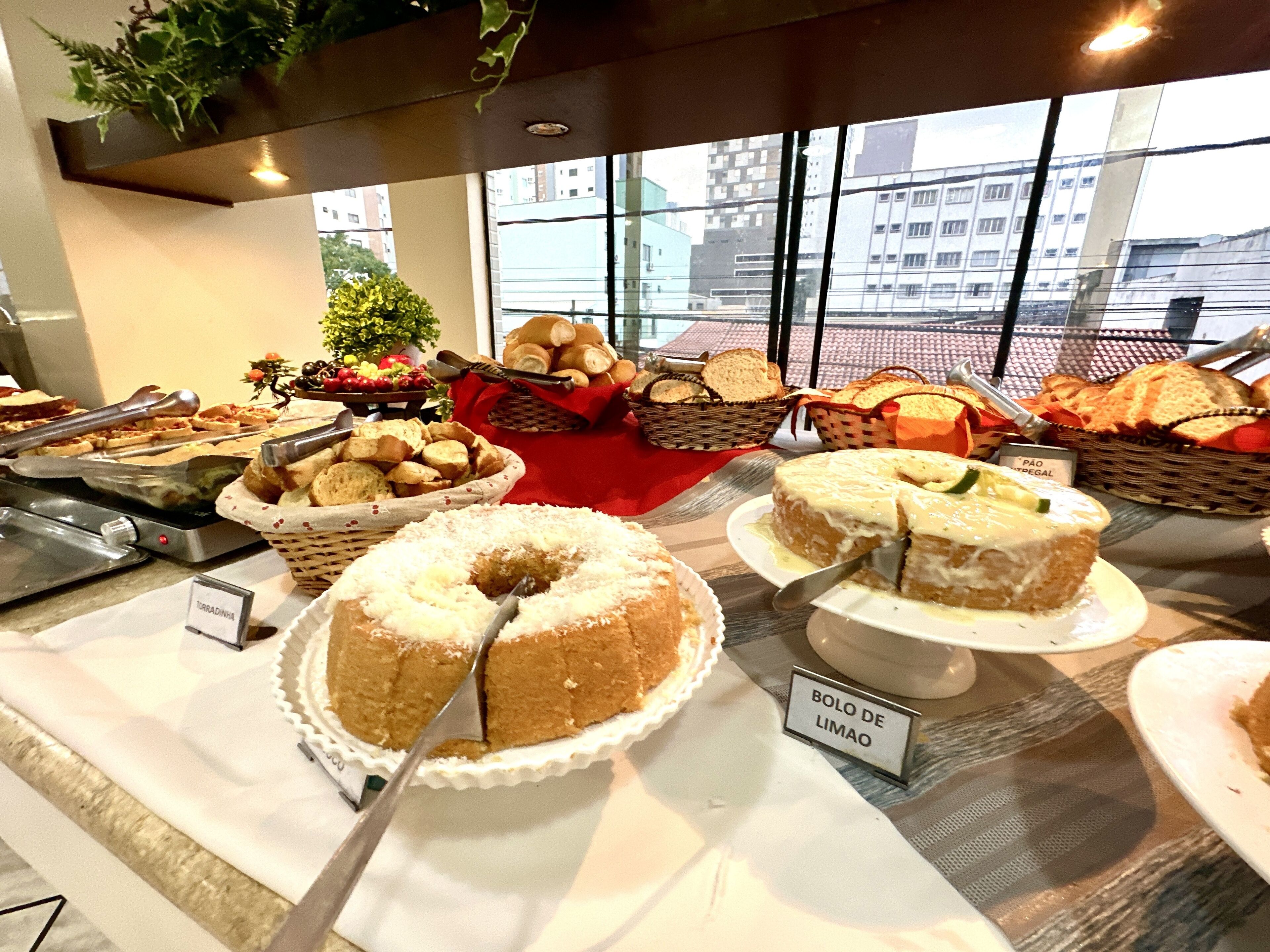 Un buffet proposant divers plats, notamment du pain, des gâteaux, et une pancarte indiquant « Bolo de Limão ».