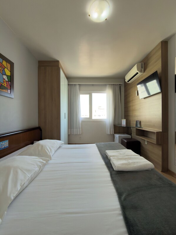 A hotel room with a large bed, a TV mounted on the wall, and a window with curtains.