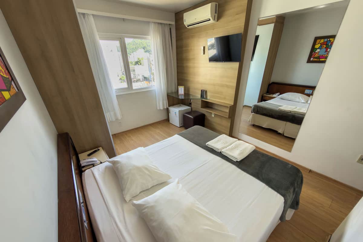 A hotel room with a bed, a desk, a chair, a TV, and a window with curtains.