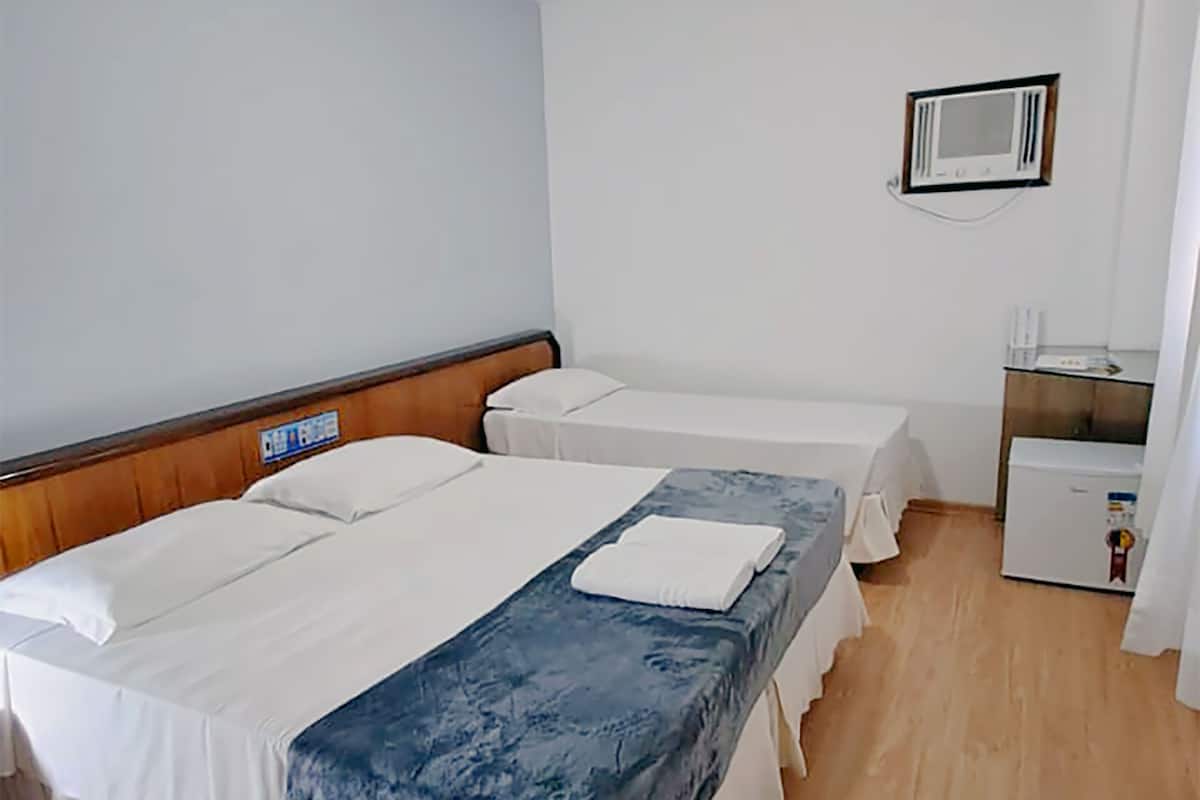 A hotel room with two beds, wooden flooring, a small kitchenette, and a white wall.