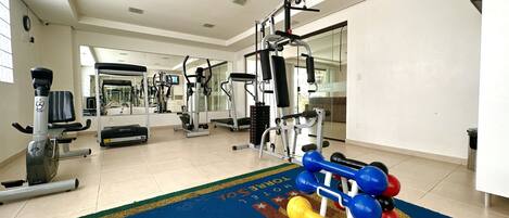 A gym with exercise equipment, a blue mat, and a mirror.