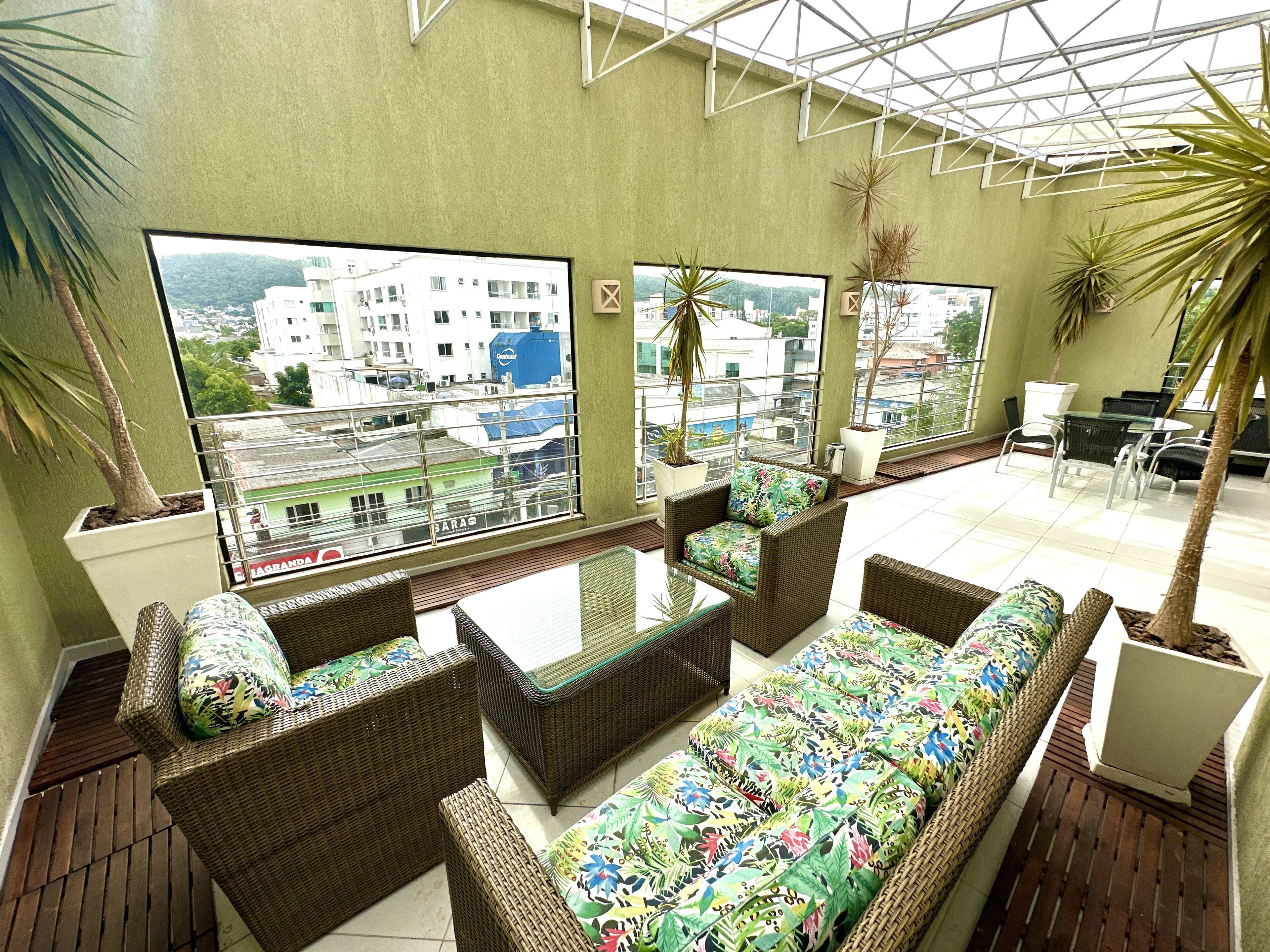 Terraza en la azotea con mobiliario de mimbre, ventanas amplias y plantas en macetas.