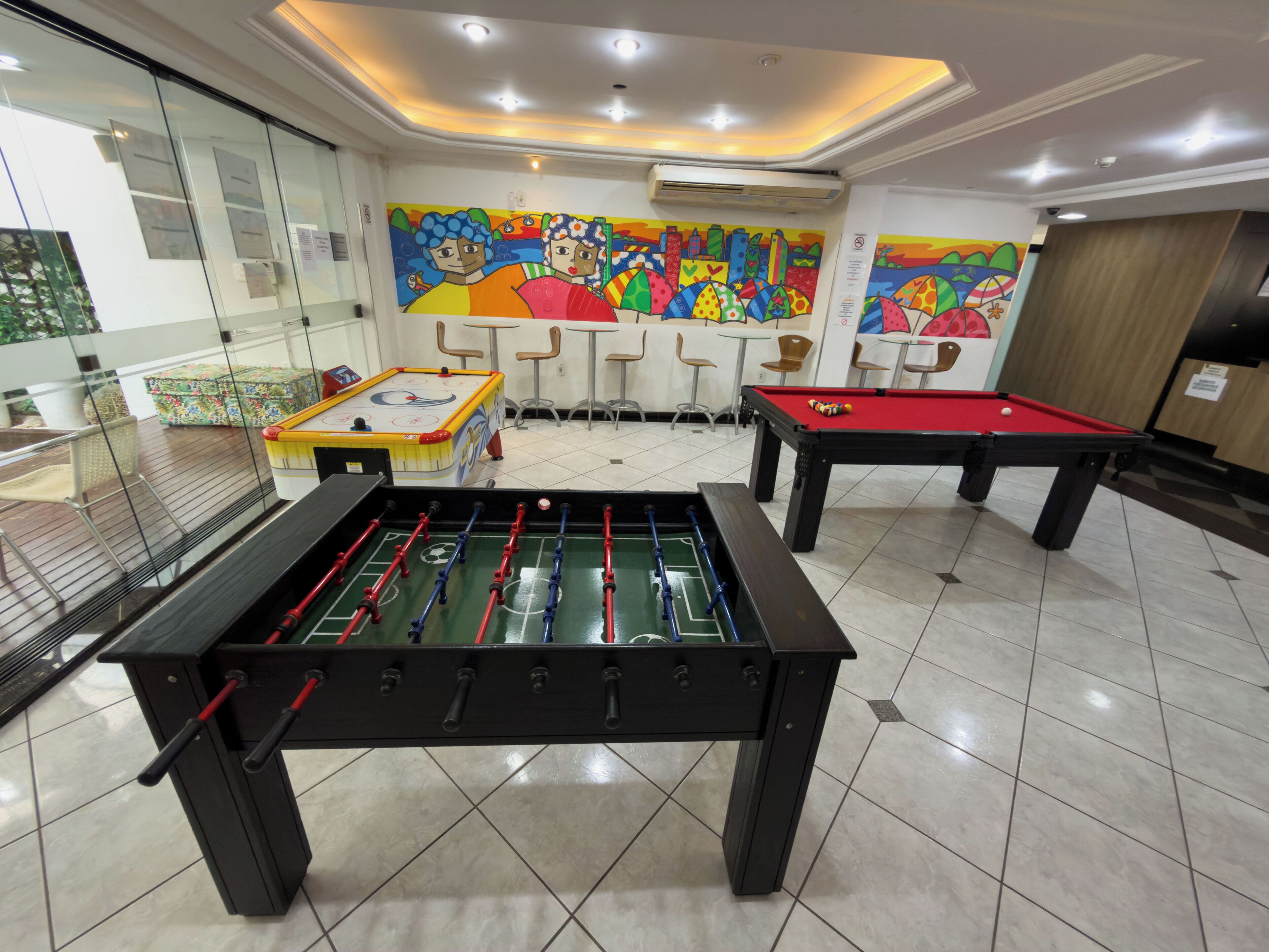 Une pièce équipée d’un baby-foot, d’une table de billard et ornée d’une fresque murale aux couleurs vives.