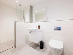 A modern bathroom with a white sink, toilet, and a glass shower enclosure.