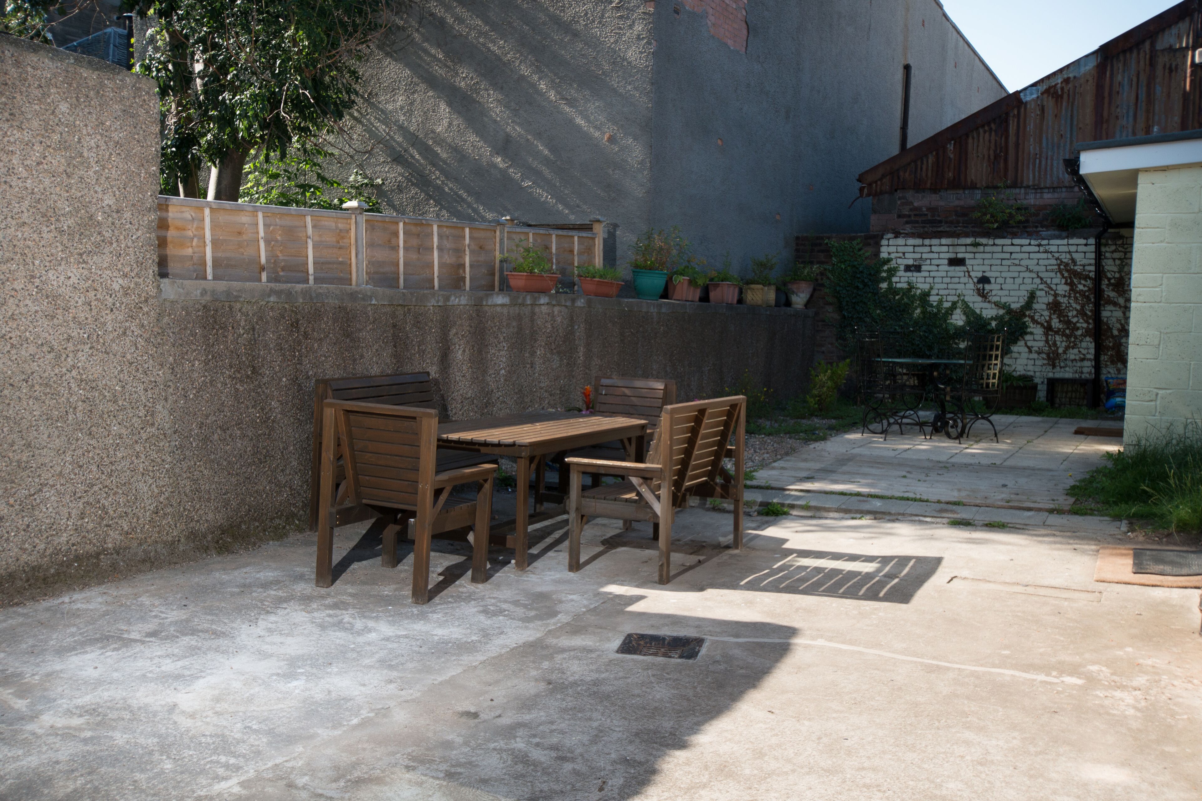 An outdoor patio with a wooden table and chairs, potted plants, and a concrete floor.